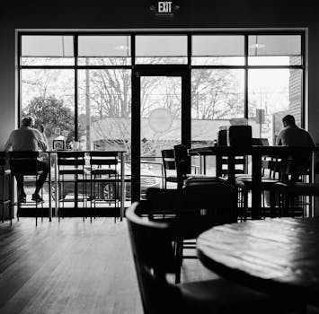 A serene black and white photograph capturing the calm ambiance of a cafe with patrons sitting alone.