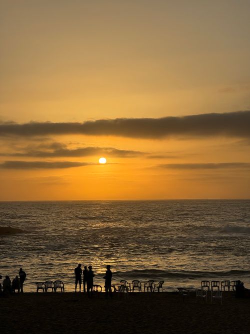 Free Silhouettes gather by the ocean at sunset in Oualidia, capturing an enchanting moment on the Moroccan coast. Stock Photo