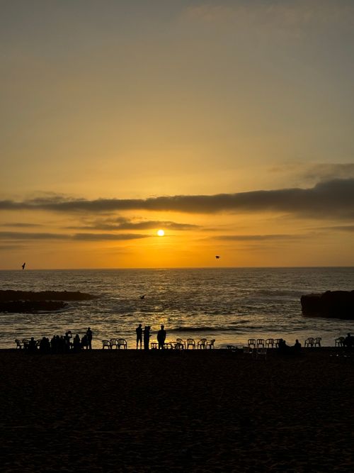 Free Silhouetted figures enjoy a tranquil sunset over the ocean at a Moroccan beach. Stock Photo