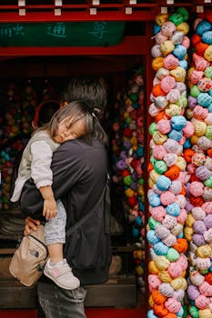 A father carries his sleeping child at a colorful Japanese temple adorned with prayer balls.