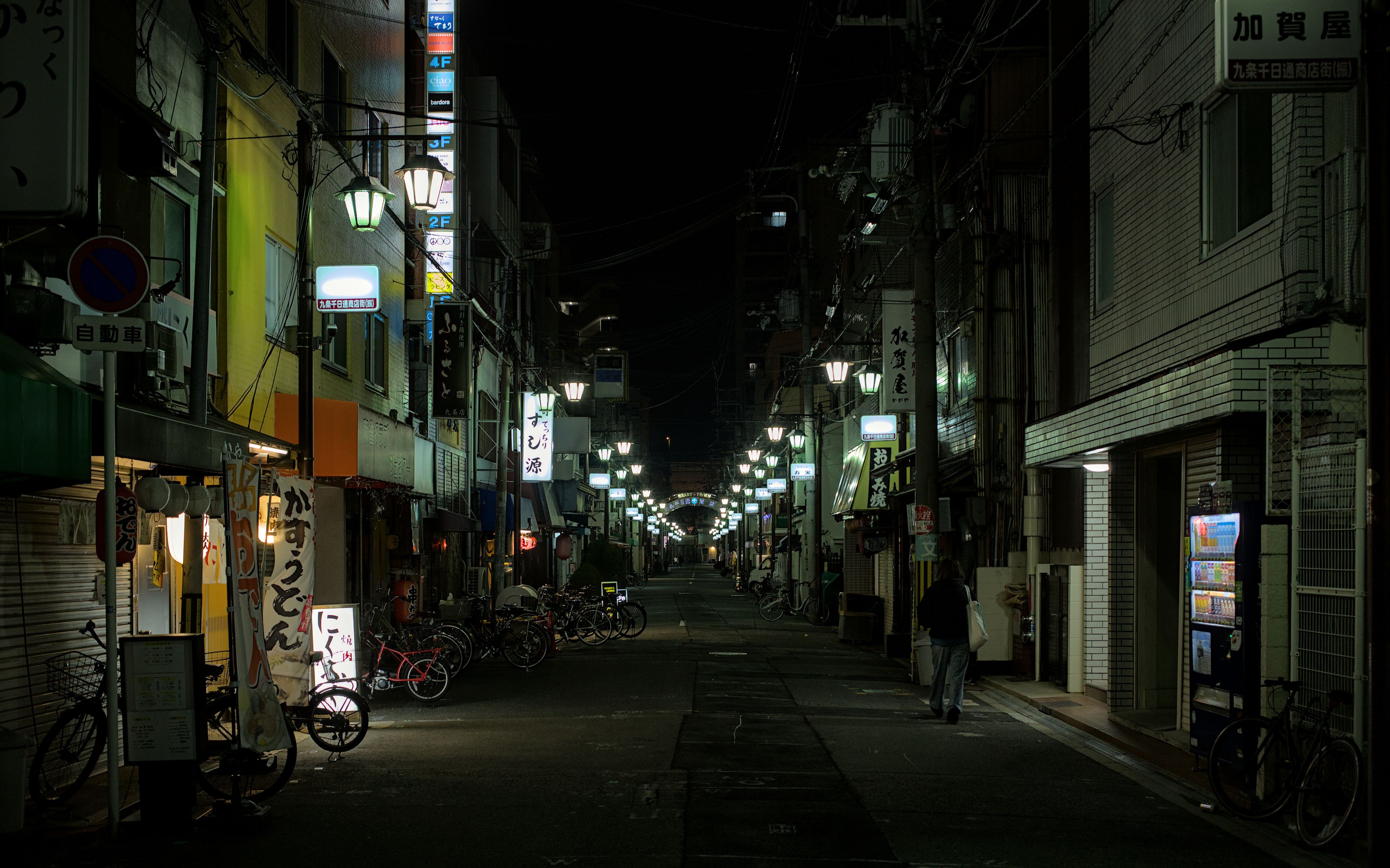 Dimly lit urban street in Osaka, featuring bicycles and neon signs on a quiet night.