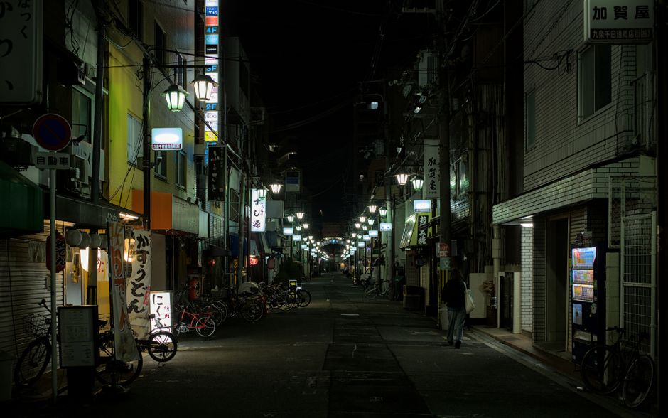 Dimly lit urban street in Osaka, featuring bicycles and neon signs on a quiet night.