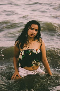 一位年轻美丽的女子在海浪中摆姿势，展现出夏日氛围和热带风情