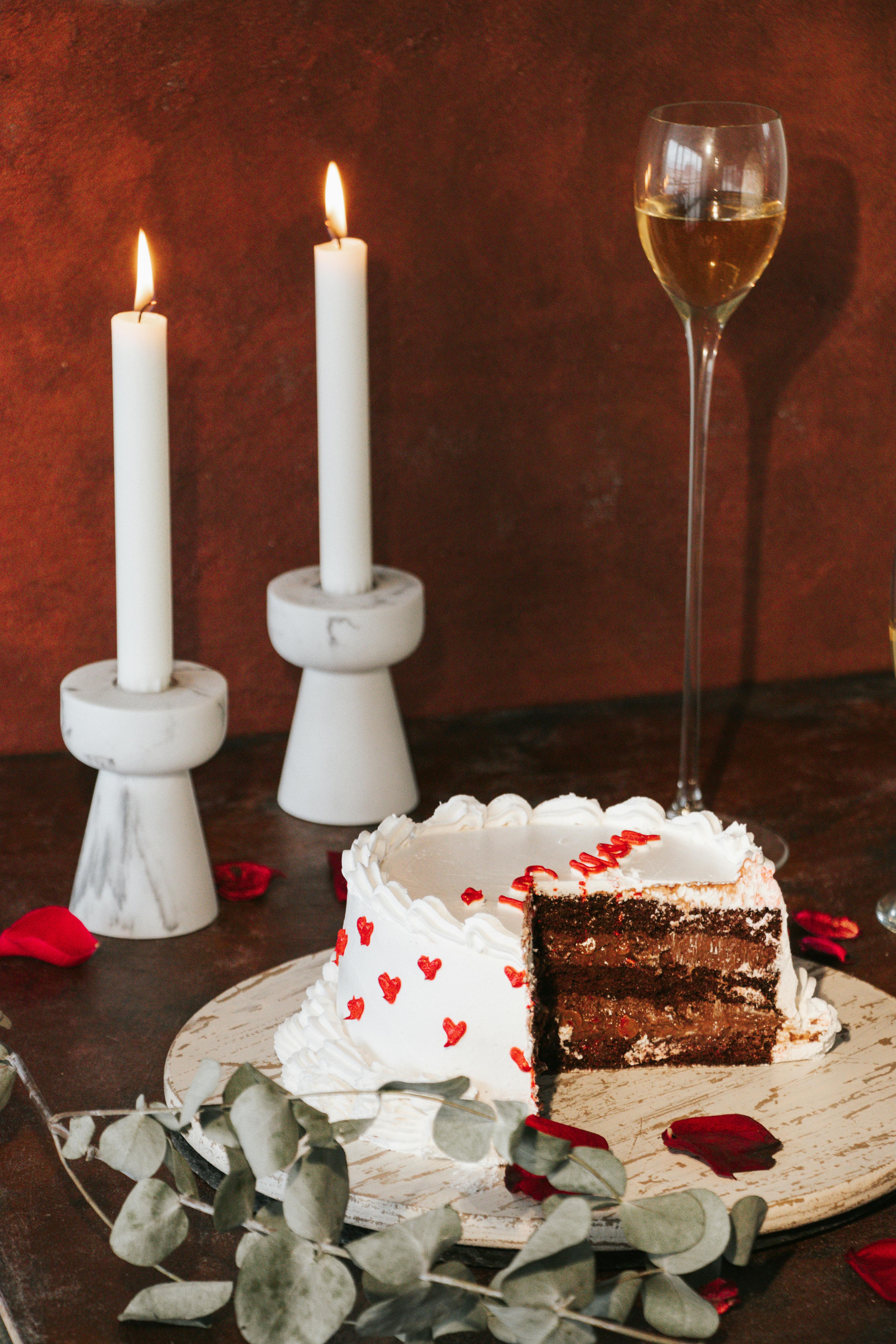 Chocolate cake with white icing and heart decor beside romantic candlelight.