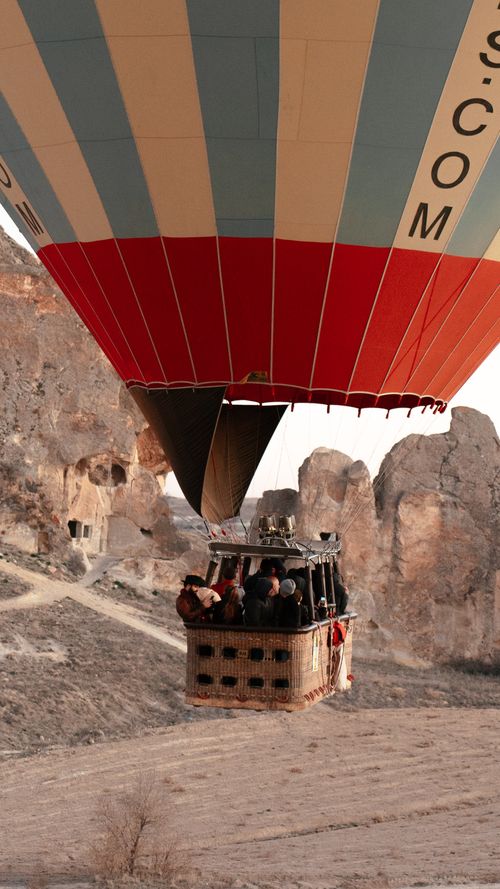 Free A vibrant hot air balloon with passengers soaring over a rugged landscape. Stock Photo