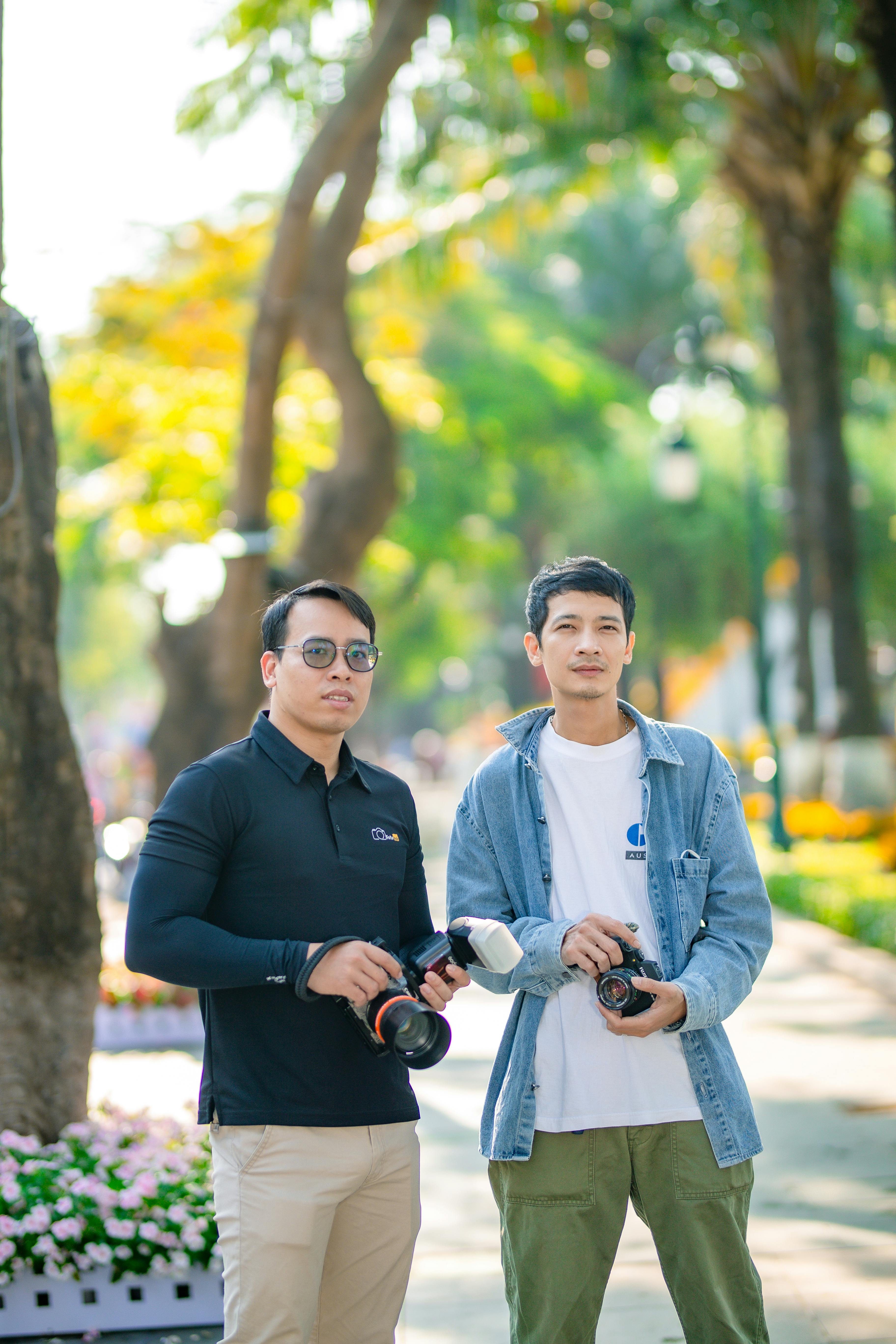 Two young photographers with cameras in a vibrant park setting.