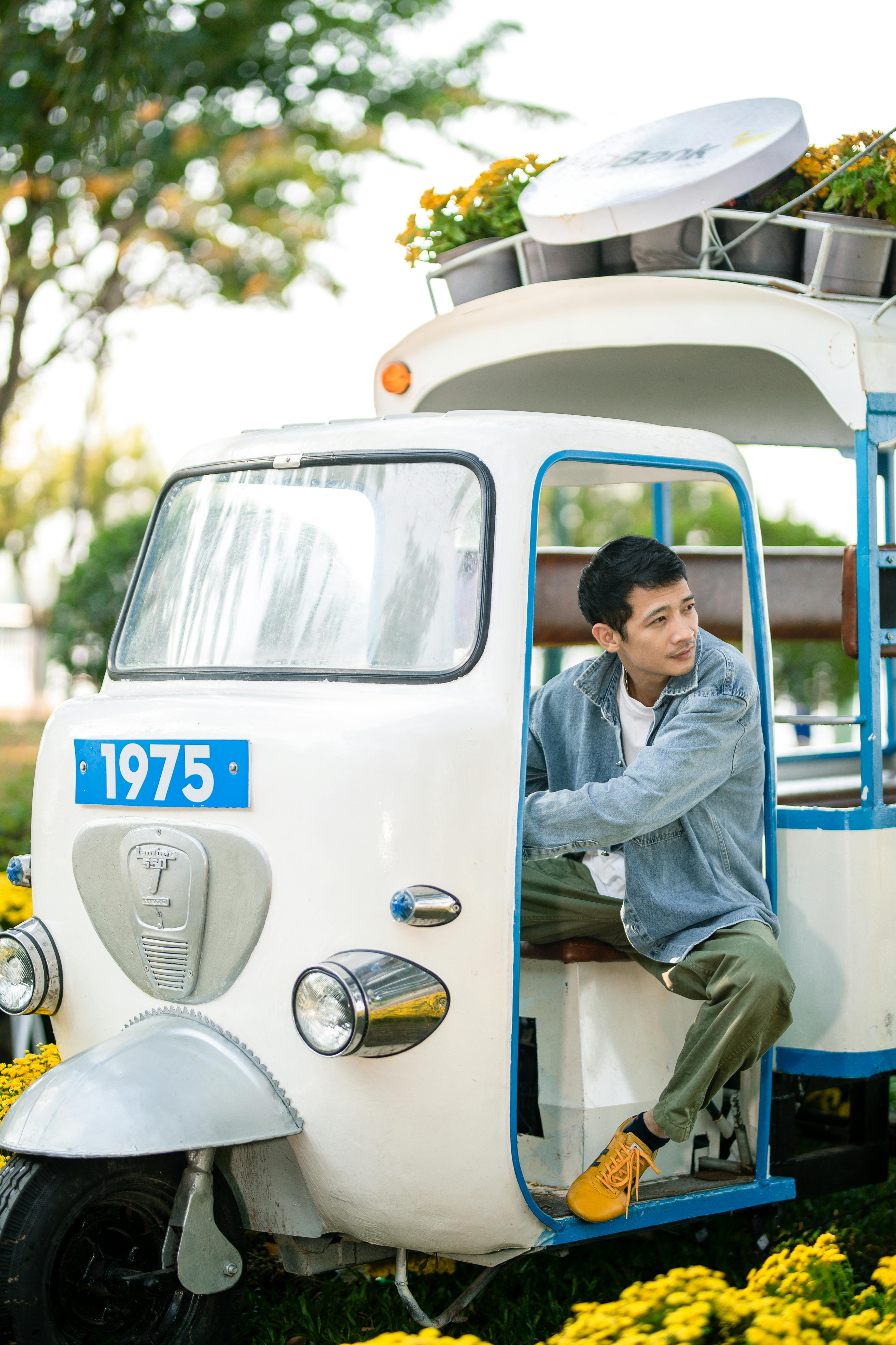 Young man in a vintage rickshaw amidst vibrant flowers, enjoying a sunny day outdoors.
