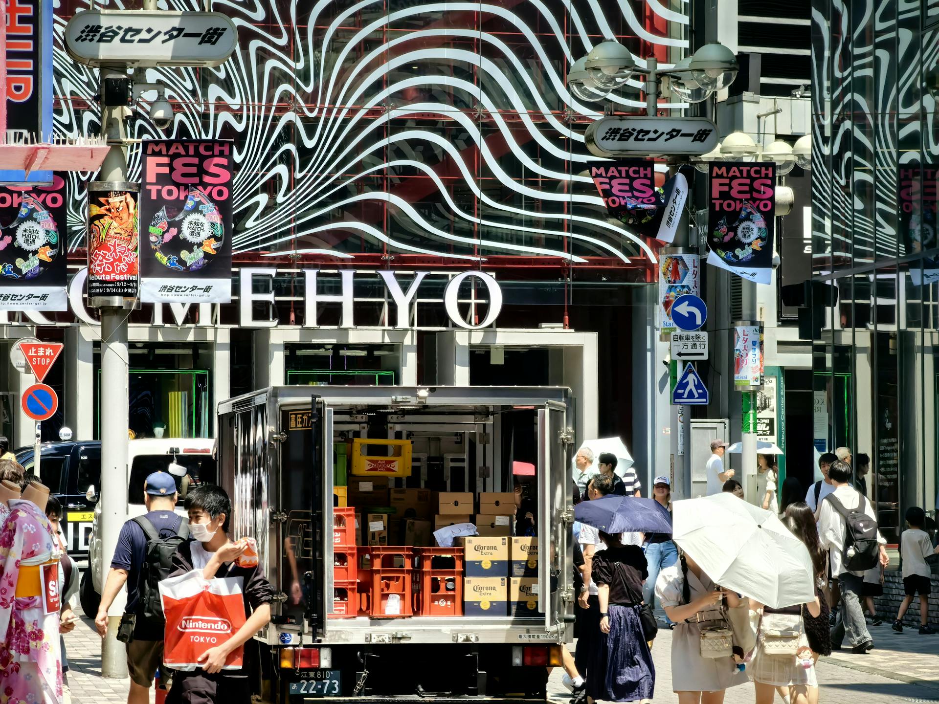 Busy street scene in Shibuya, Tokyo, with shoppers and delivery truck under vibrant signage.