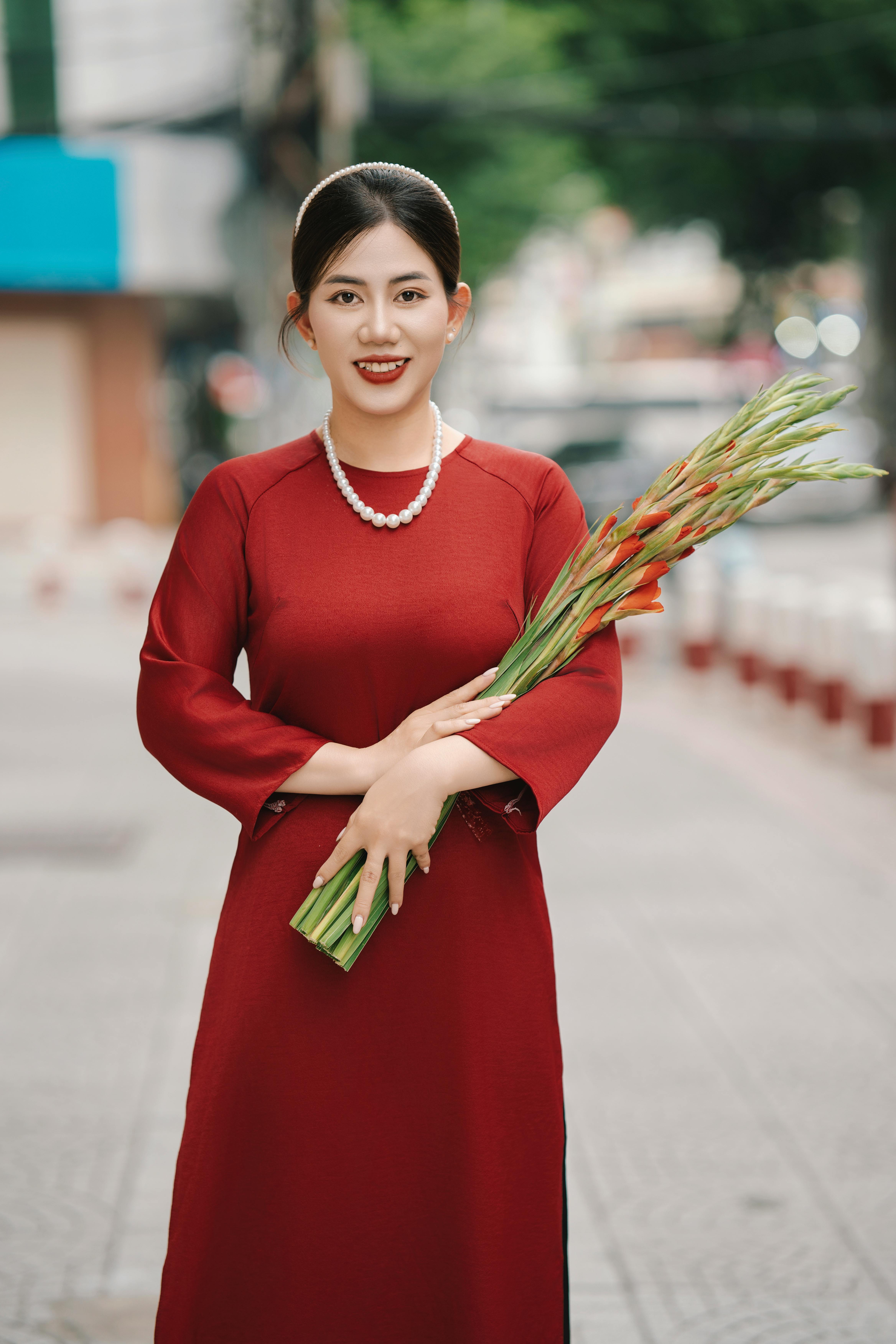 bezplatná Usmívající se žena v červených šatech drží kytici mečíků na ulici města. Základová fotografie