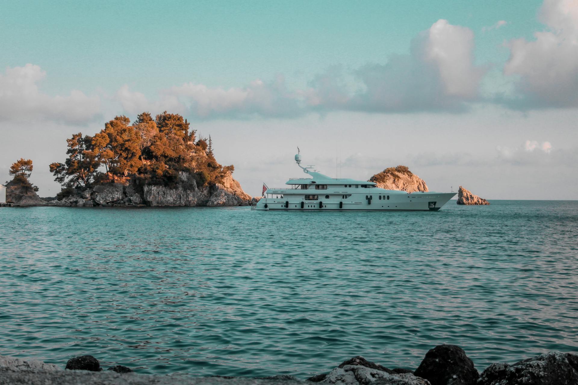 Serene view of a luxury yacht near a tranquil Greek island at sunrise.