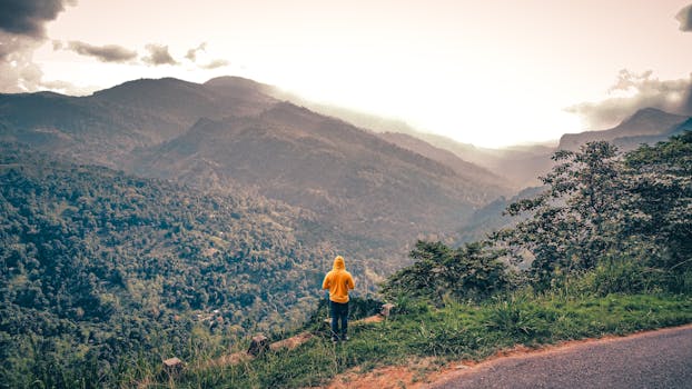 Person in yellow hoodie admiring a stunning mountain landscape during sunset.