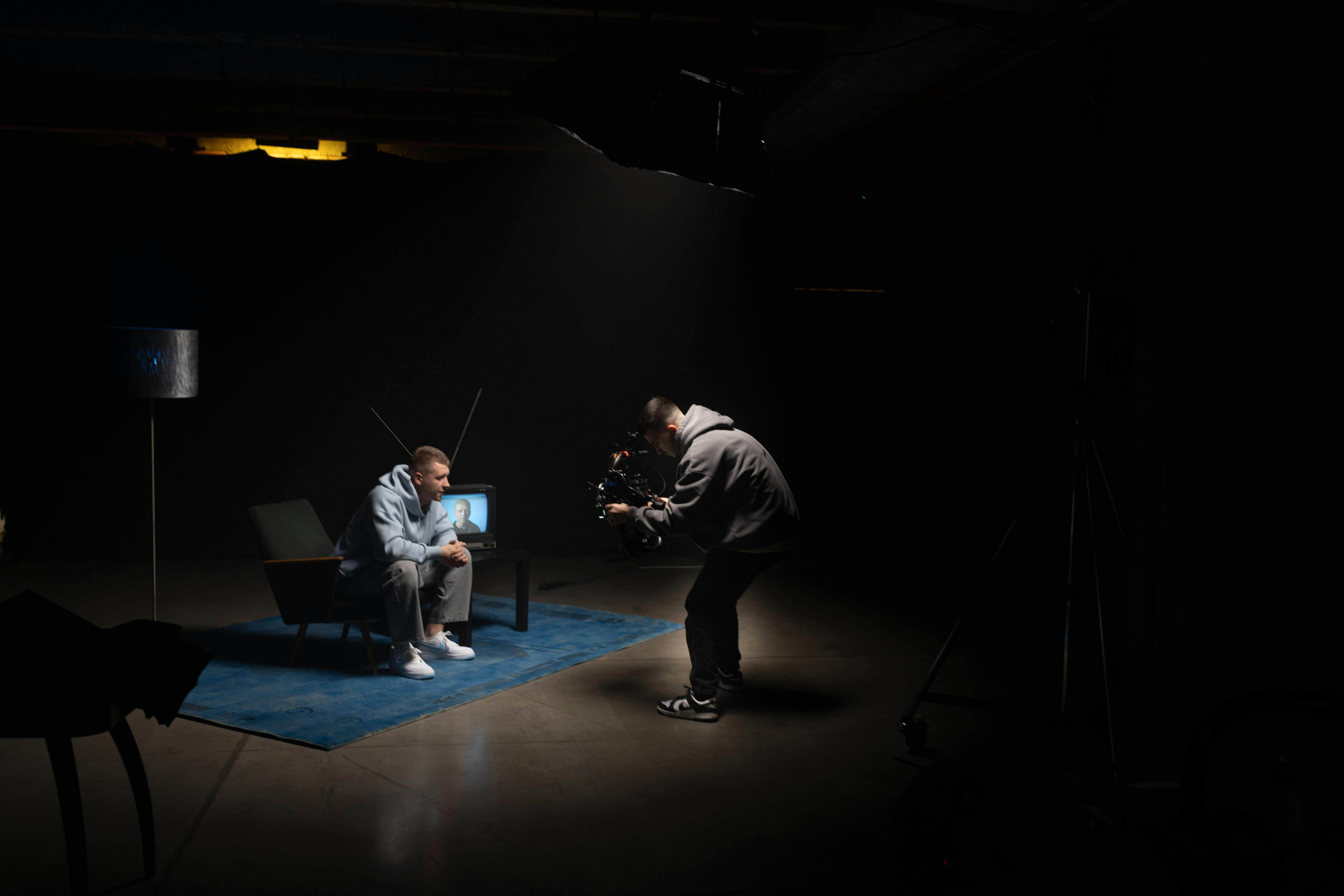 Gratis Riprese di produzione cinematografica in interni, con il direttore della fotografia che filma un attore seduto, luci da studio. Foto a disposizione