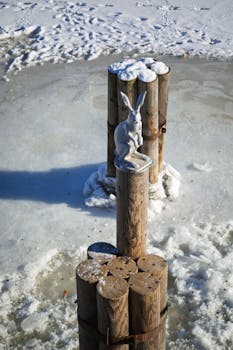 A rabbit sculpture perched on poles over a frozen lake in winter.