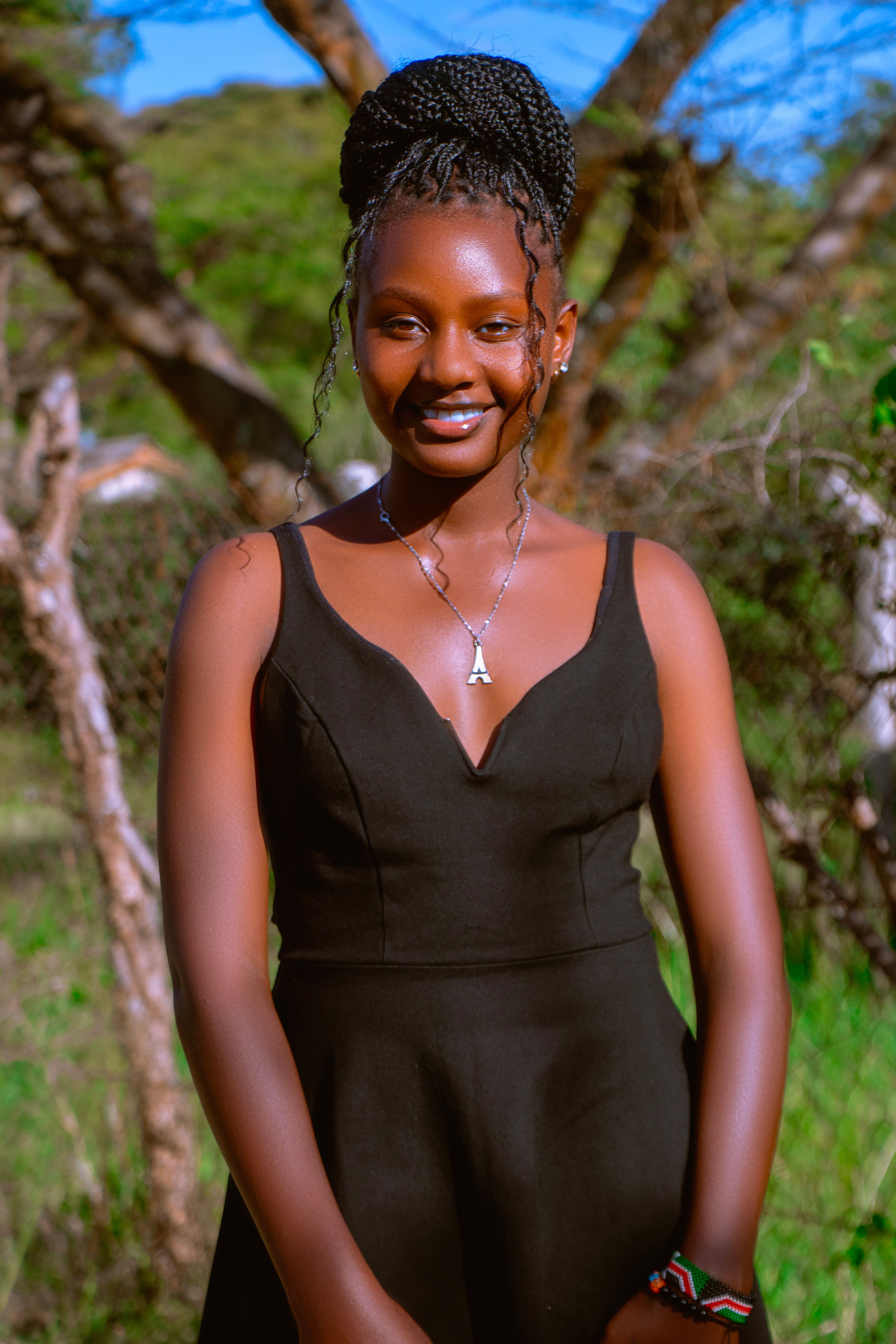A vibrant portrait of a smiling woman in a black dress set in the lush outdoors of Machakos, Kenya.