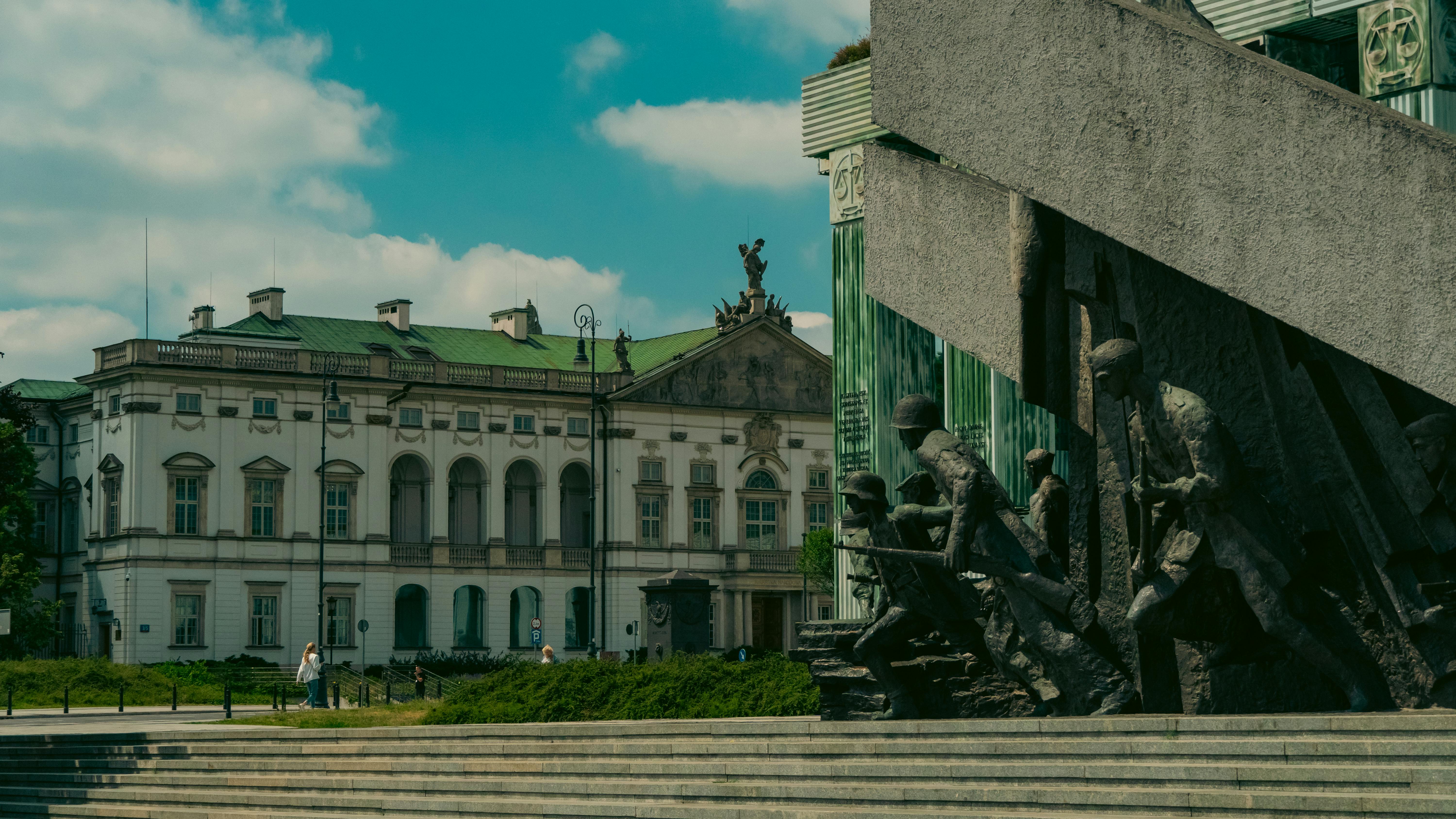 War memorial sculpture with soldiers beside a historic building under a blue sky
