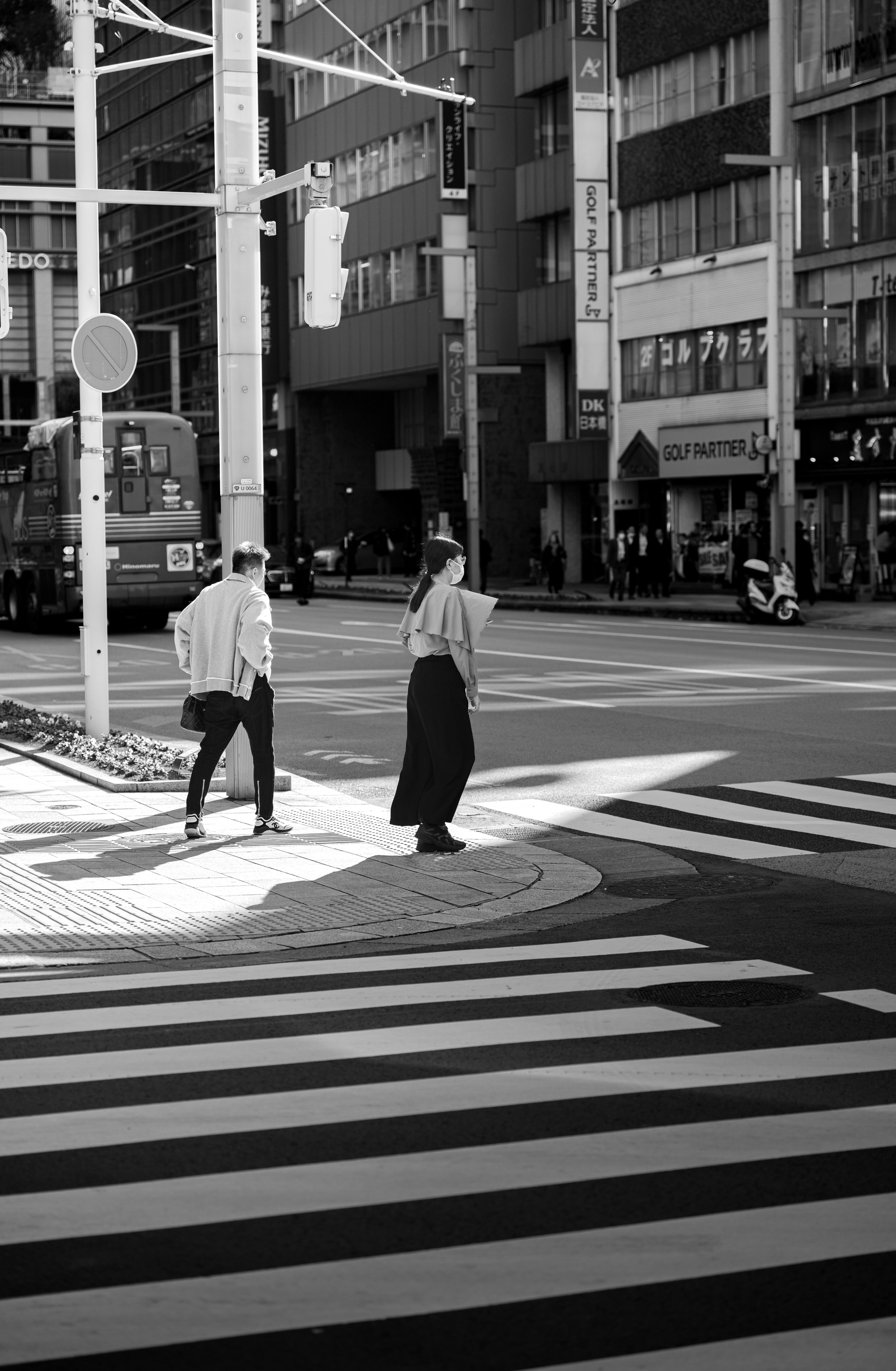 Two adults crossing a Japanese city street in monochrome tones.