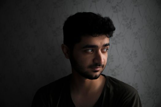 Contemplative young man in low light setting, looking thoughtful.