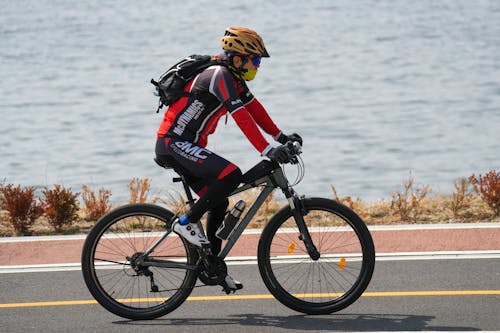 gratis Een fietser met veiligheidsuitrusting fietst op een zonnige dag langs de waterkant, een voorbeeld van gezonde buitenactiviteiten. Stockfoto
