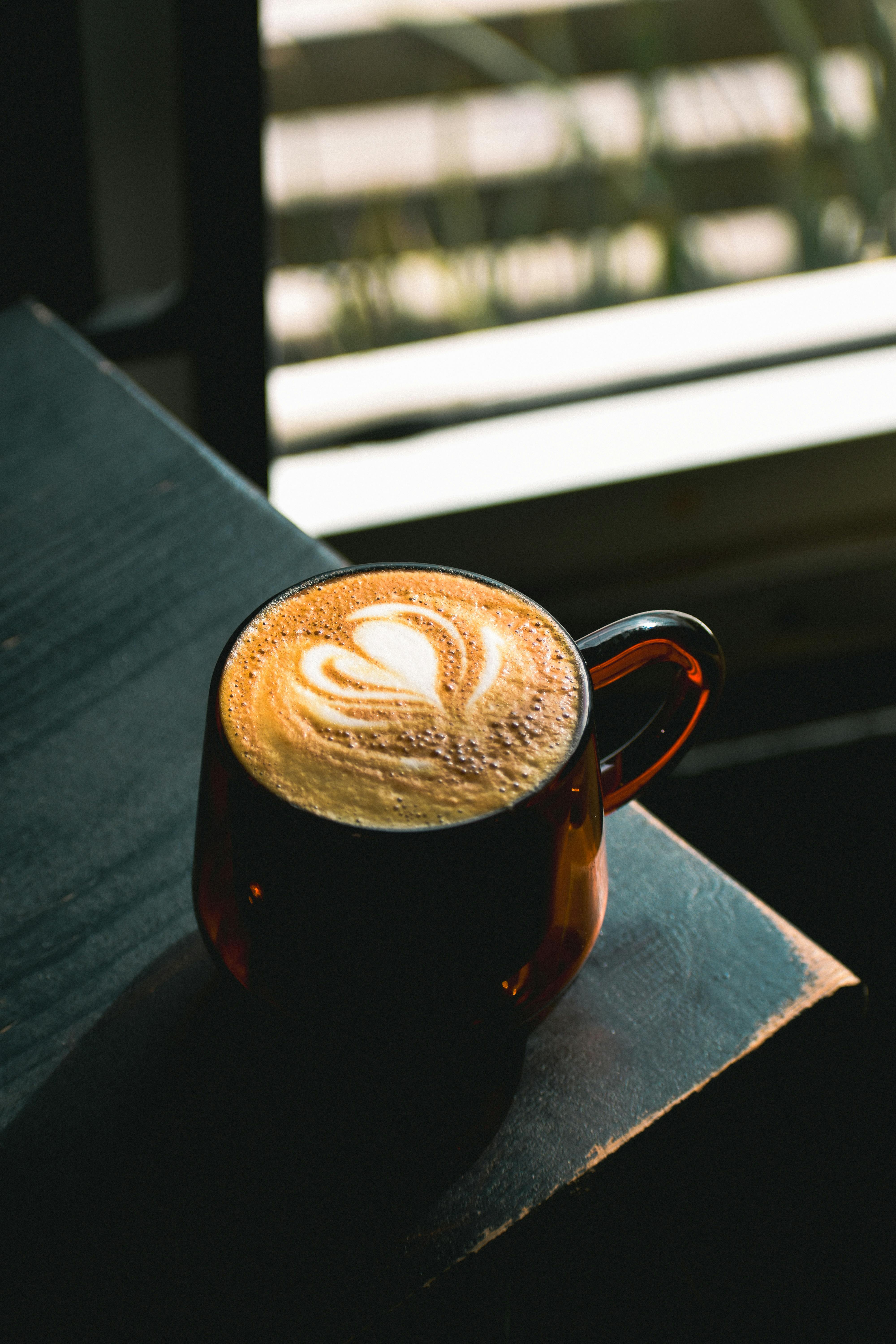 Warm café latte with heart latte art, captured by a sunny window in Tijuana.