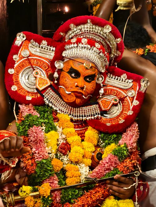 Free Vibrant portrait of a traditional Theyyam performer adorned in elaborate red and orange costume and floral garlands. Stock Photo