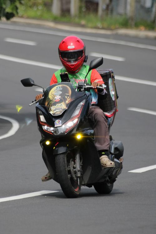 Free Motorcyclist with red helmet and delivery backpack riding on urban road. Stock Photo