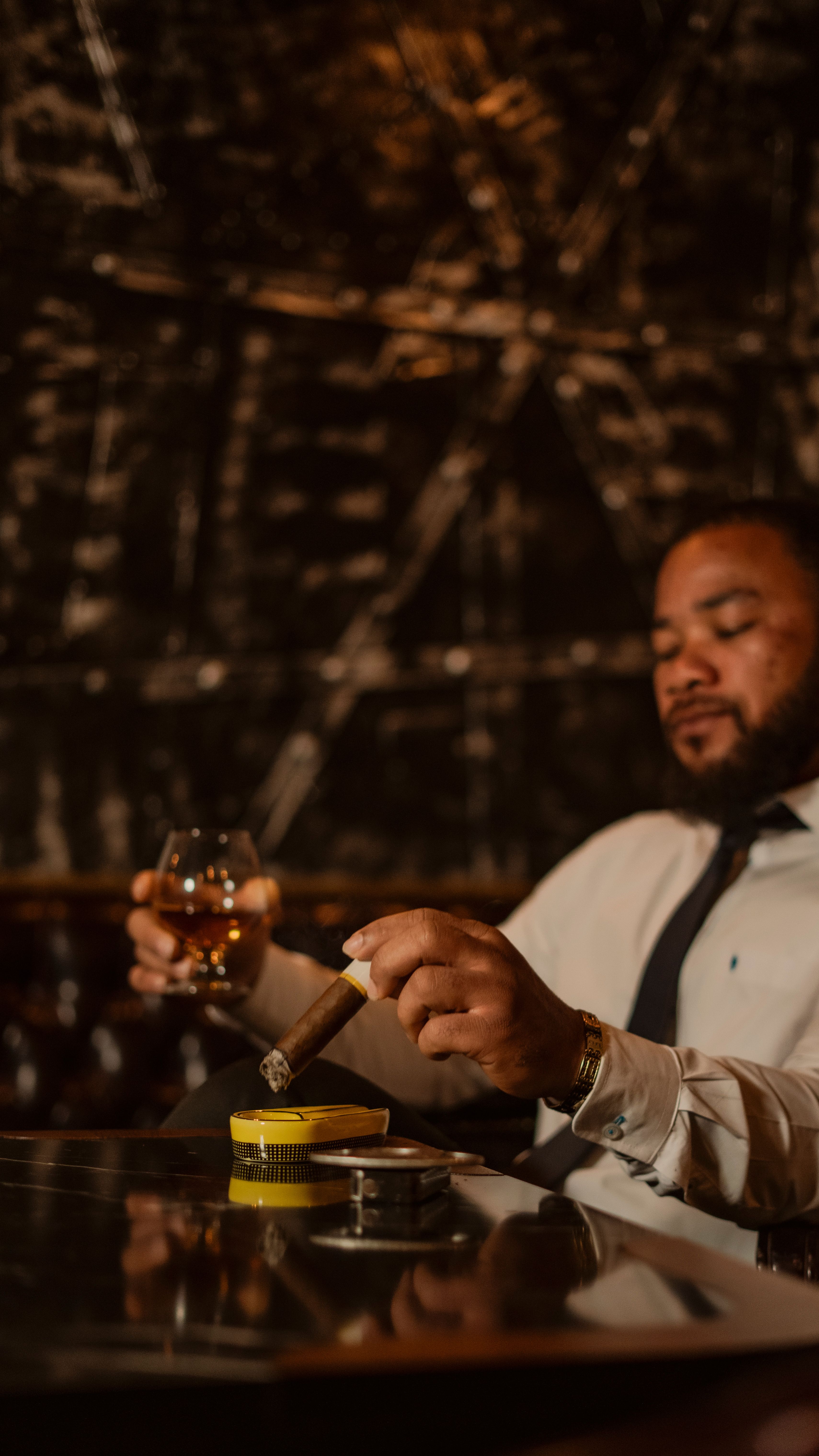 Gratis Un hombre bien vestido se relaja con un cigarro y una bebida en un sofisticado ambiente interior. Foto de stock