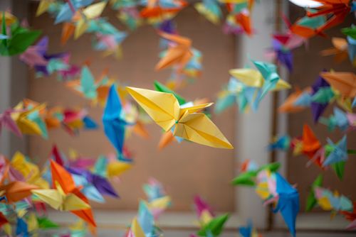 Free Vibrant origami cranes float in a serene Japanese garden setting, capturing a cultural essence. Stock Photo