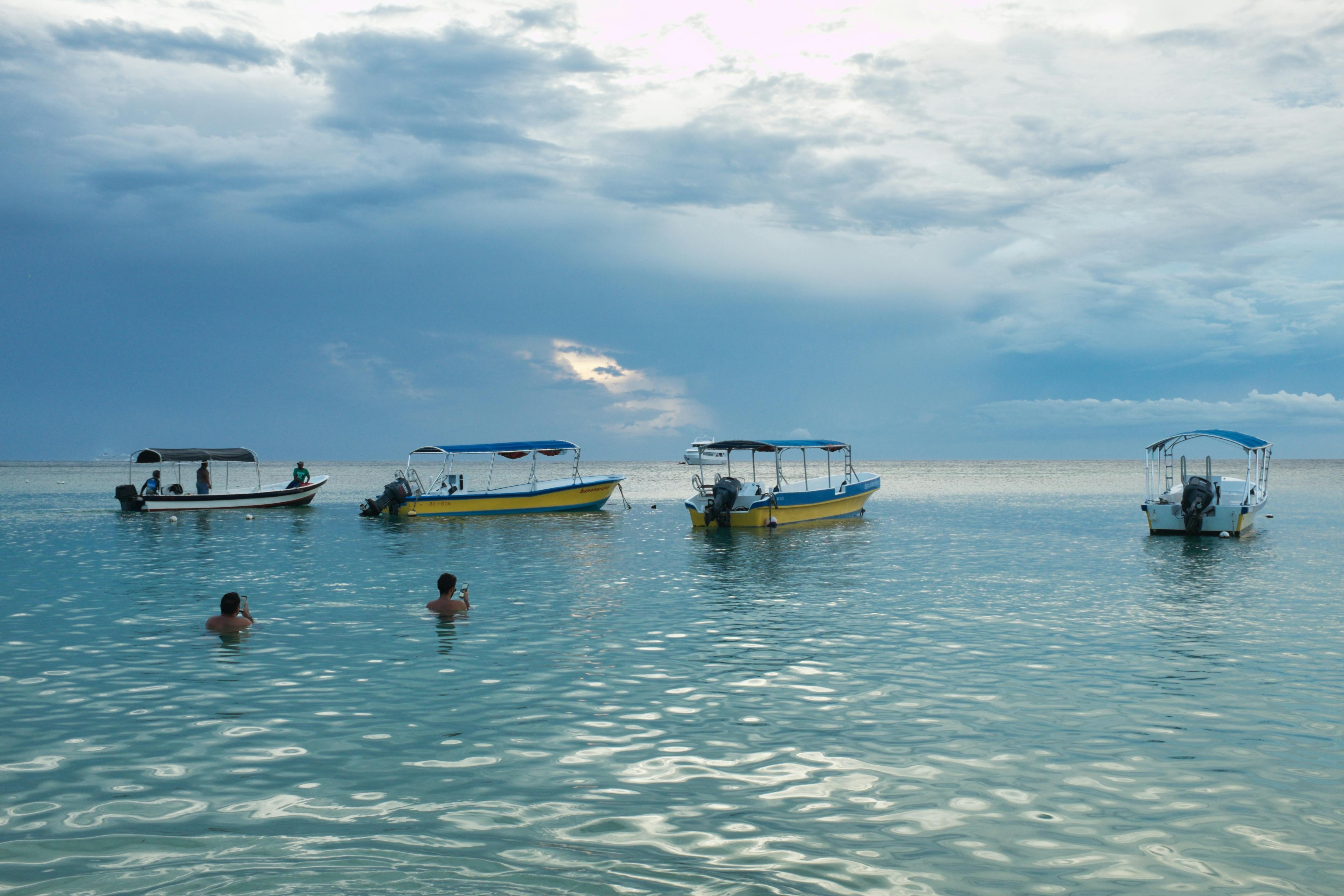 Tranquil ocean scene with boats anchored as swimmers enjoy the calm waters.