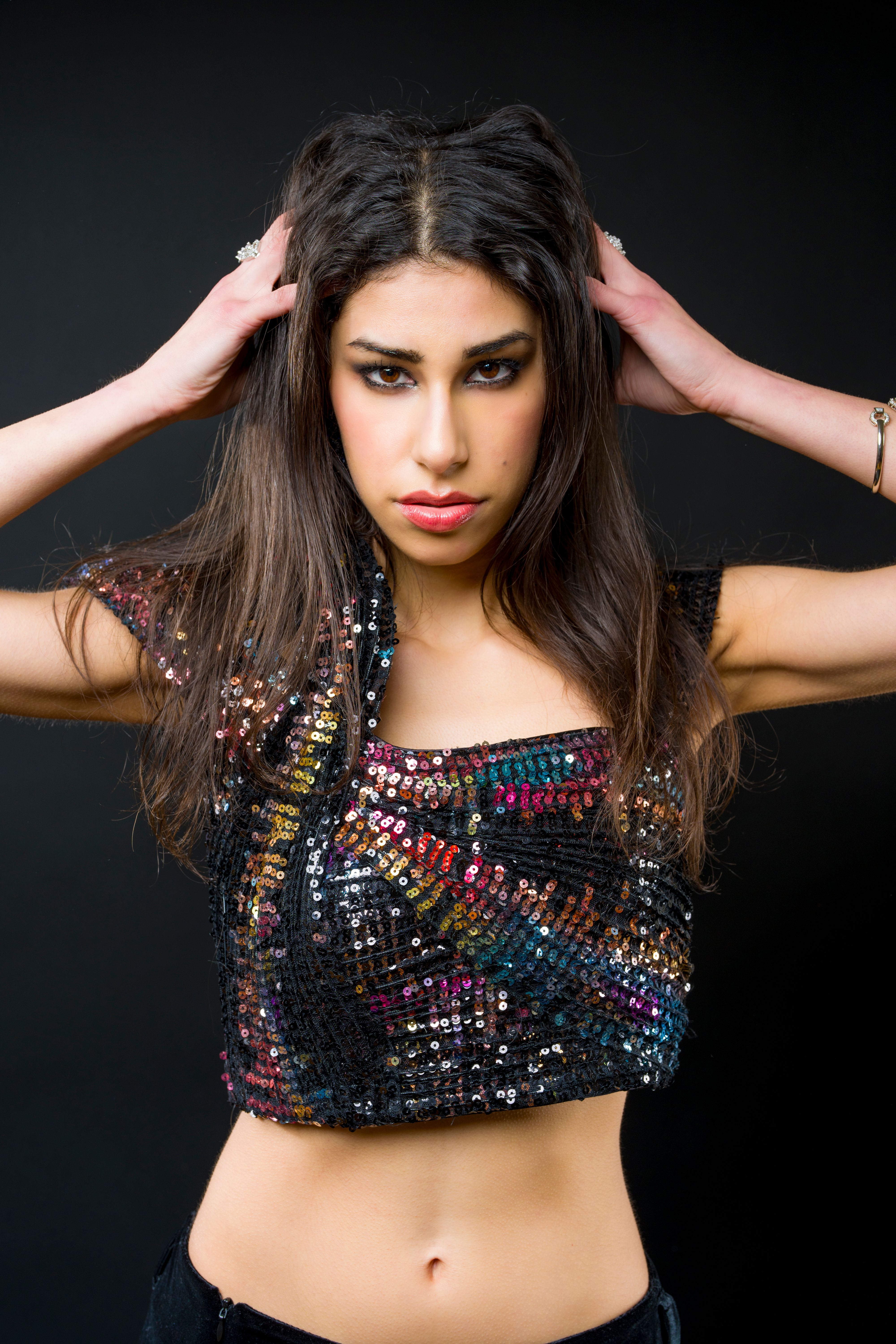Confident woman striking a pose in a vibrant sequin top against a black backdrop.