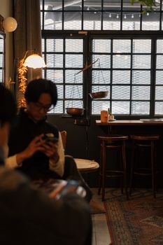 Warm cafe with a person immersed in their phone, steel windows, and rustic decor.