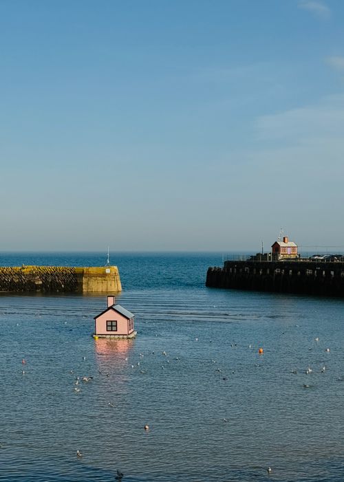 Free A solitary pink house floats in the serene waters of Folkestone harbor under a clear blue sky. Stock Photo