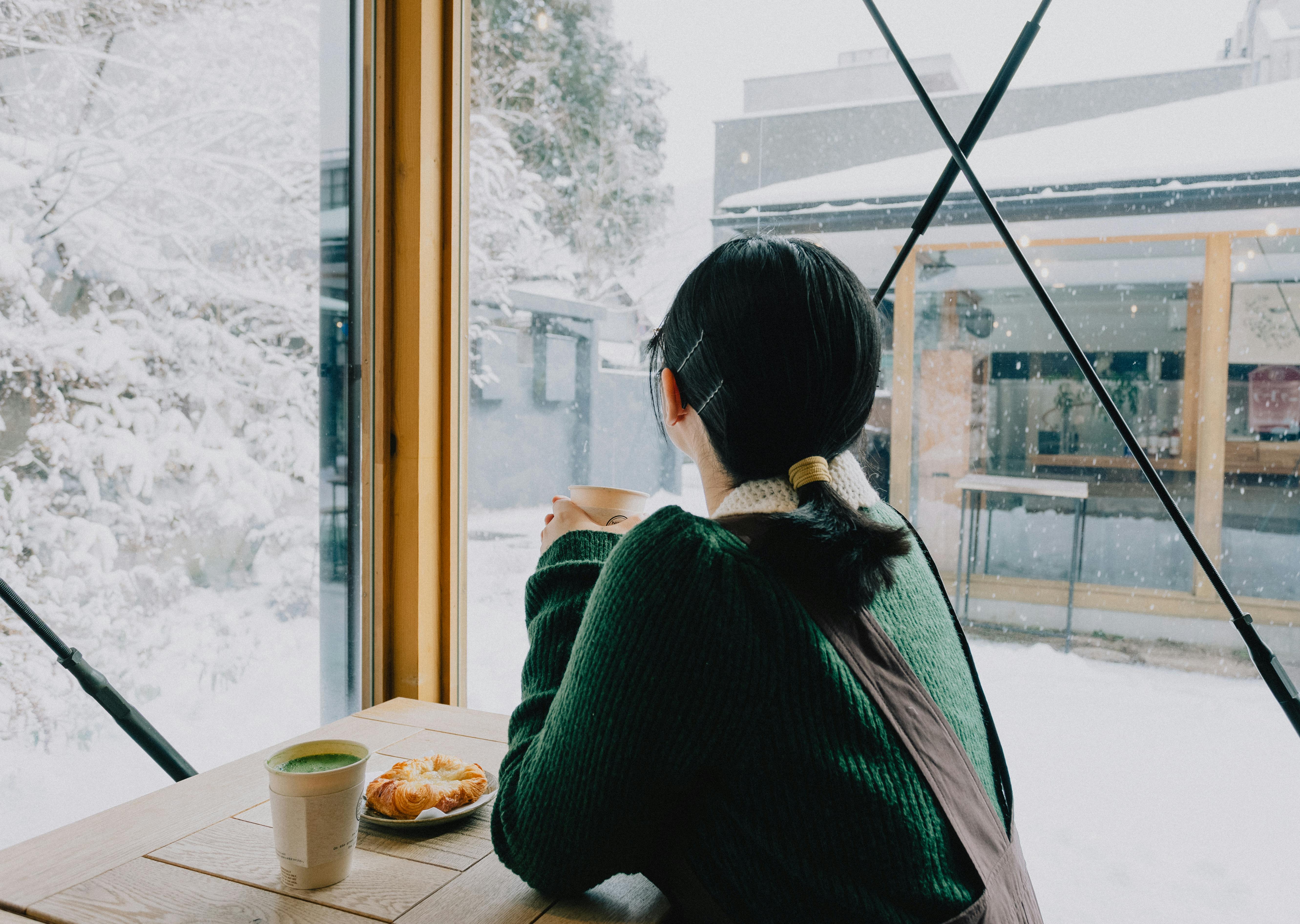 Woman enjoying coffee inside a cafe, gazing at snow-covered landscape in Nikko, Japan.