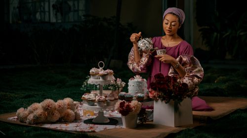 Free A woman enjoys an elegant tea party outdoors with floral arrangements and cupcakes. Stock Photo