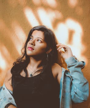 一位留着长发的年轻女子身着休闲装，在户外倚着纹理墙摆姿势