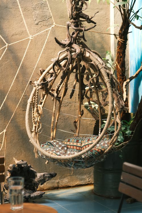 Free Sunlit indoor setting with a rustic rope swing chair and patterned cushion, exuding a bohemian vibe. Stock Photo