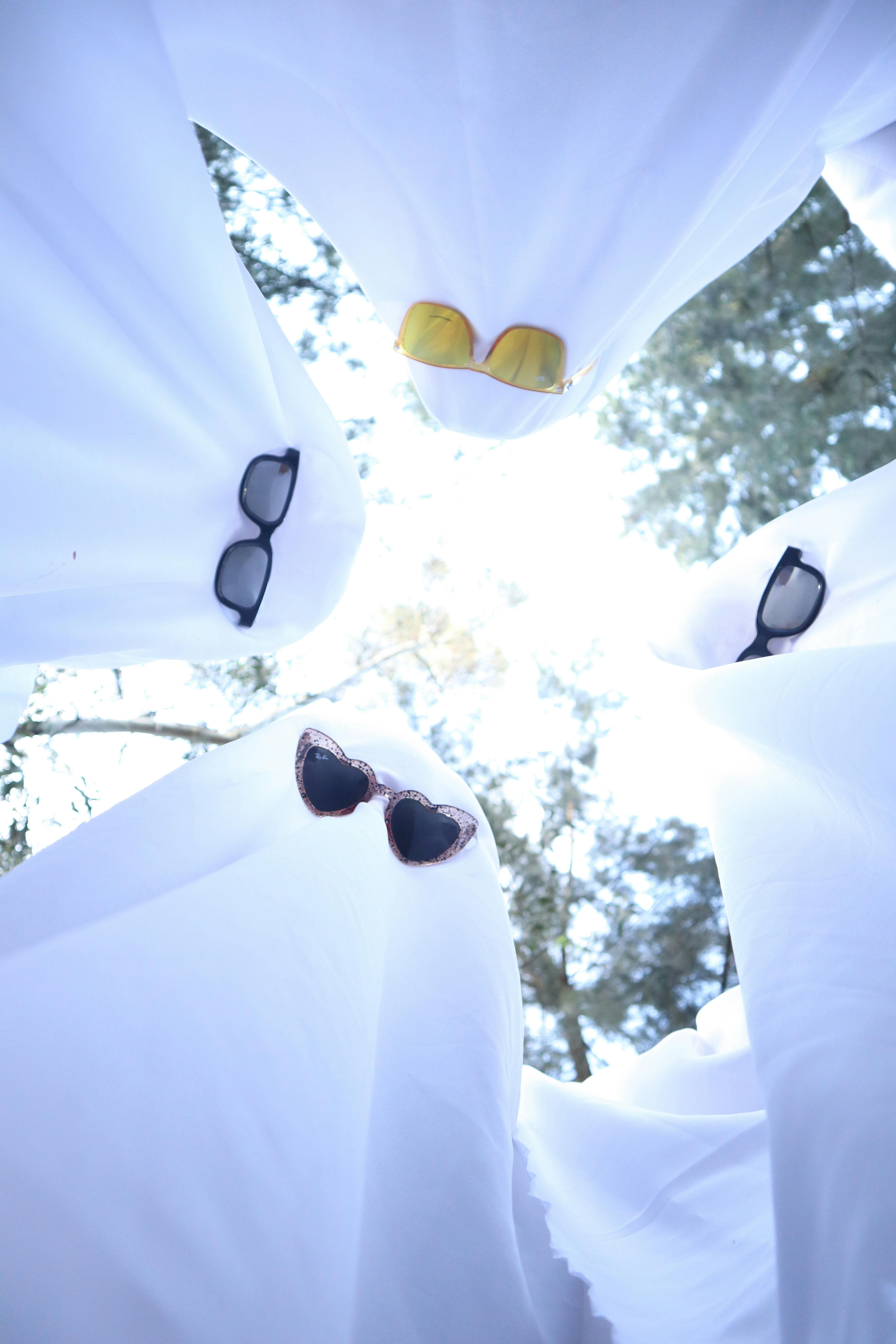 Creative shot of ghost costumes with sunglasses viewed from below against a bright sky.