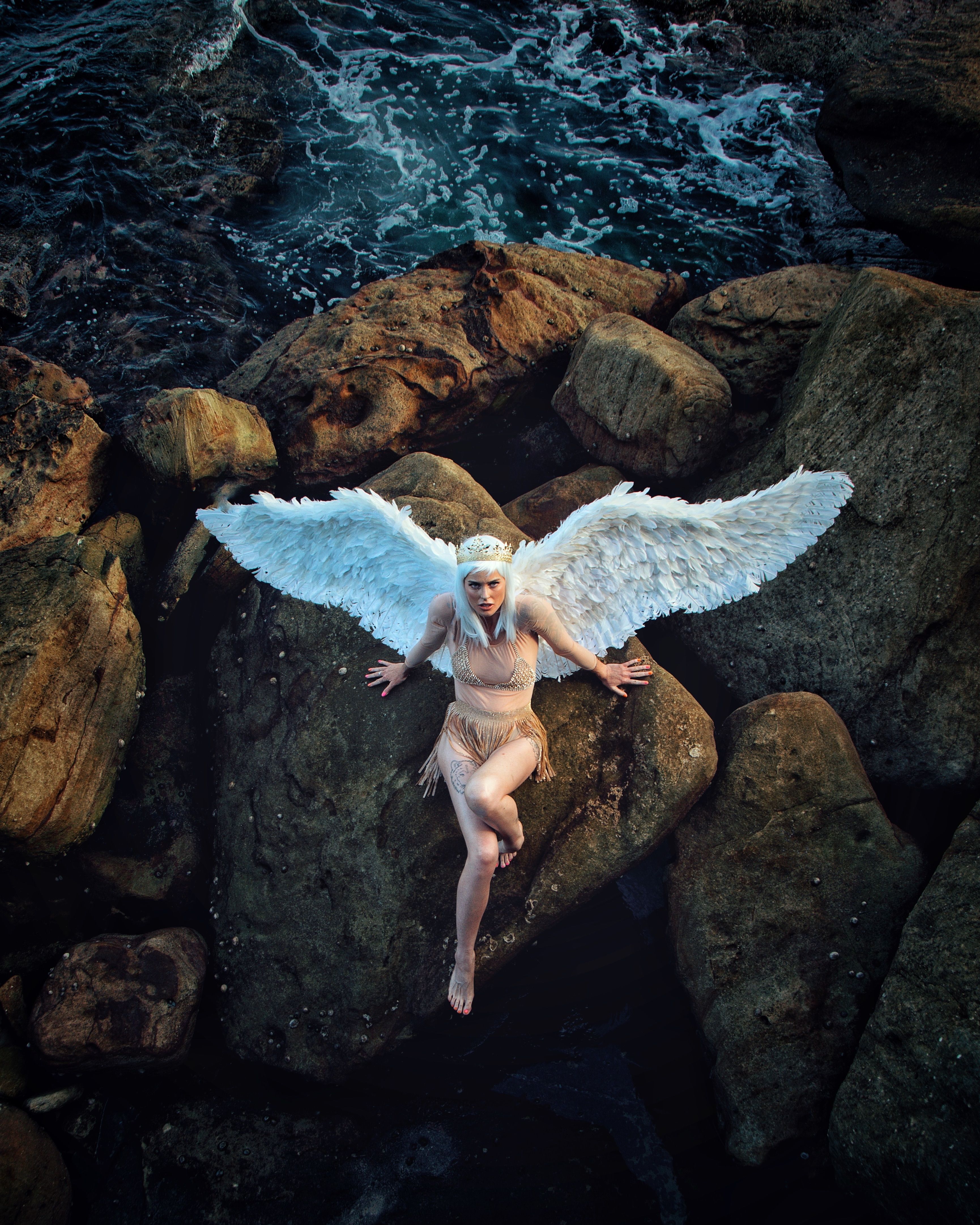 A conceptual portrait of an angelic figure with wings, posed on coastal rocks in Sydney, creating a surreal, artistic scene.