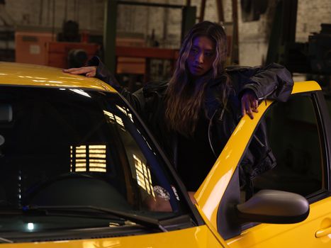 A person leaning on a yellow car in a dimly lit garage, creating a moody atmosphere.