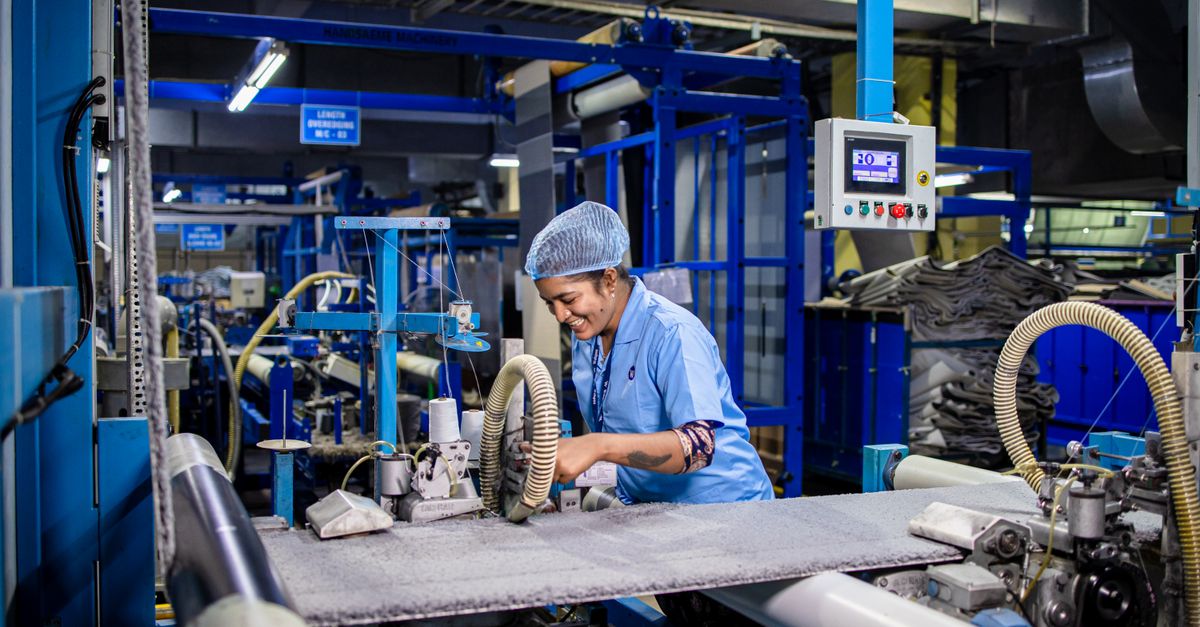 Indian female factory worker smiling while operating complex textile machinery in an industrial setting.