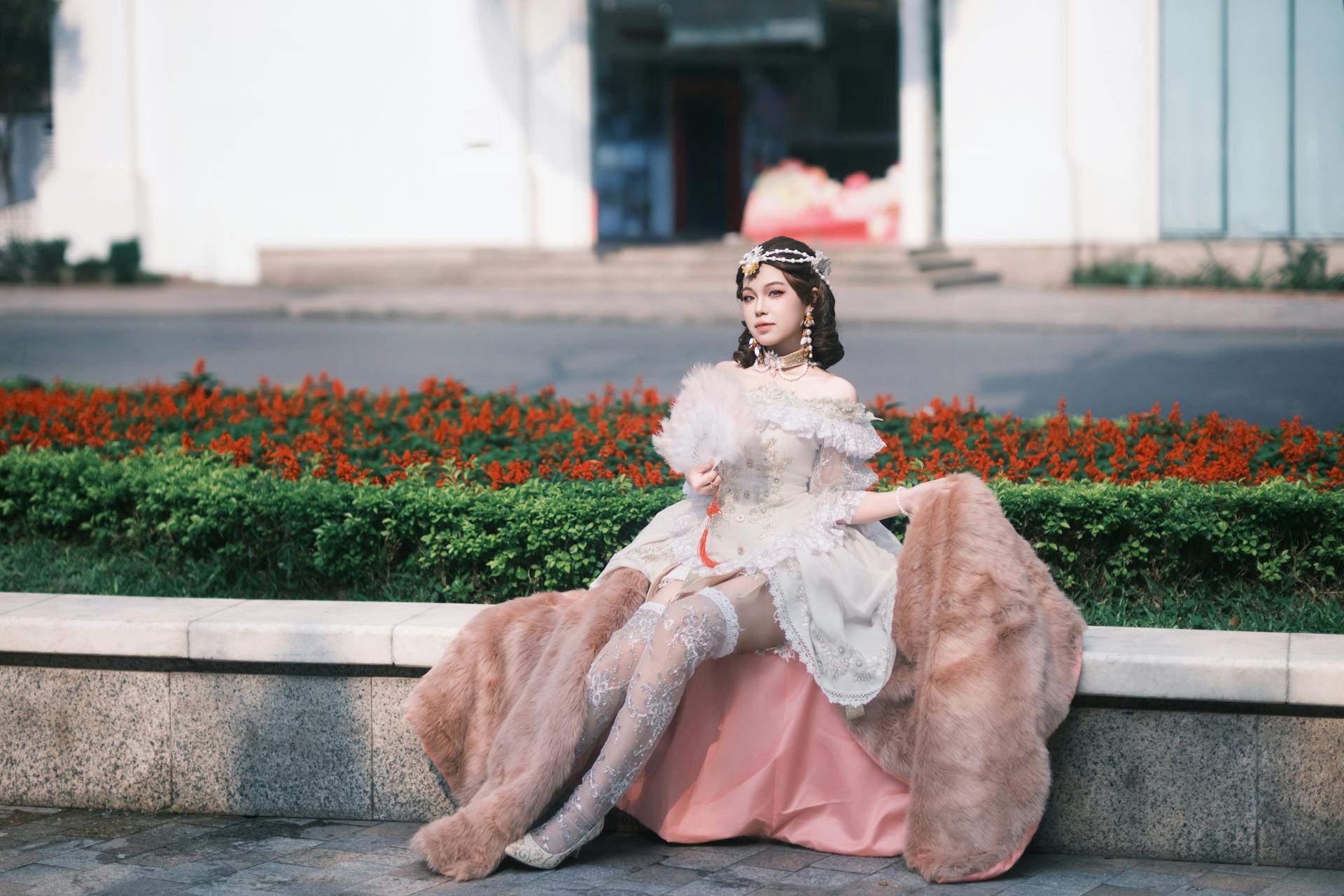 A woman dressed in a vintage Victorian costume sits gracefully outdoors, holding a delicate fan.