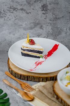 A slice of layered chocolate and vanilla cake garnished with strawberry, beautifully presented on a wooden slab.
