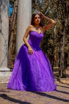 A woman in a stunning purple gown poses outdoors, embodying elegance and grace in a natural setting.