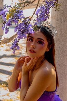 A captivating portrait of a woman in a purple dress and crown under vibrant purple flowers, exuding a fairy-tale charm.
