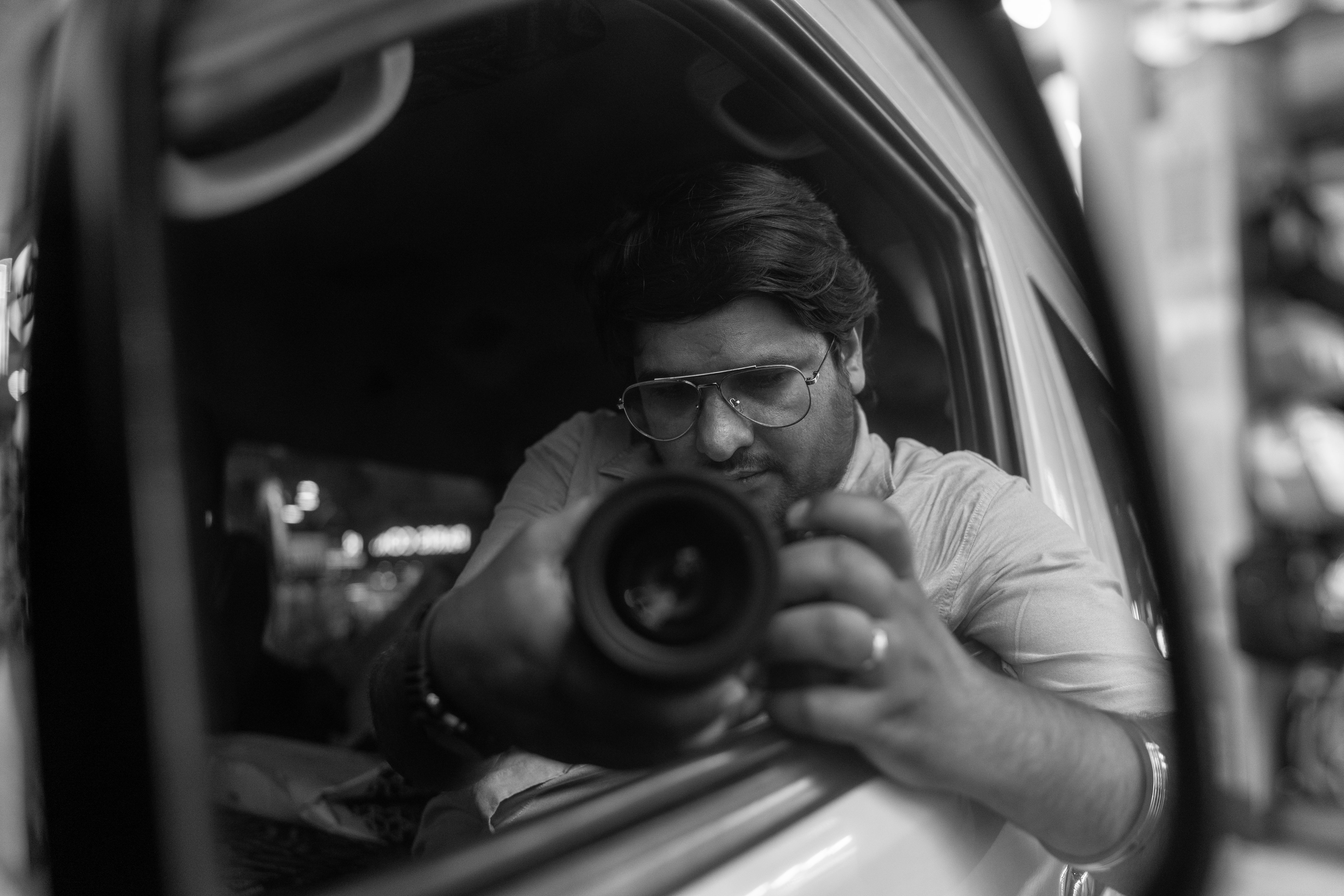 Photographer capturing self-portrait using car mirror reflection.