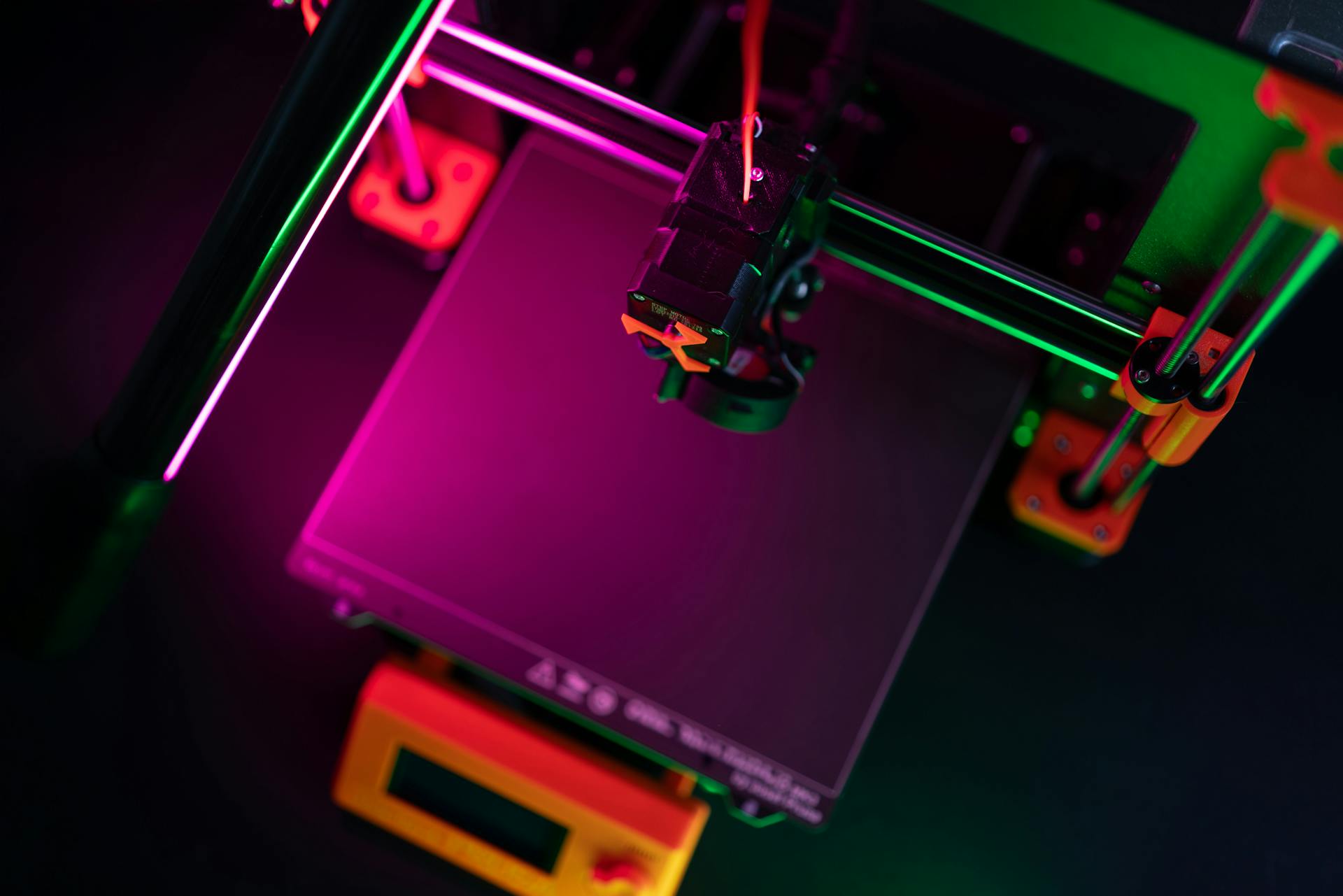 A vibrant overhead view of a 3D printer with neon lighting, emphasizing modern manufacturing.