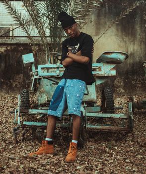 Confident young man in casual attire poses against rustic backdrop of old machinery.