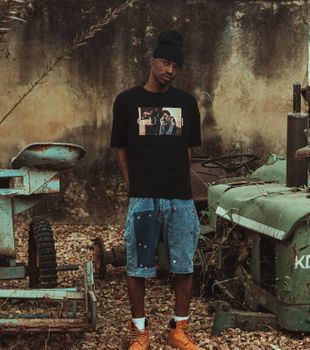 Stylish young man wearing urban clothing stands near vintage machinery outdoors.