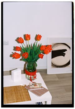 Vibrant red tulips in a glass vase on a white table in a modern interior space with art and decor.