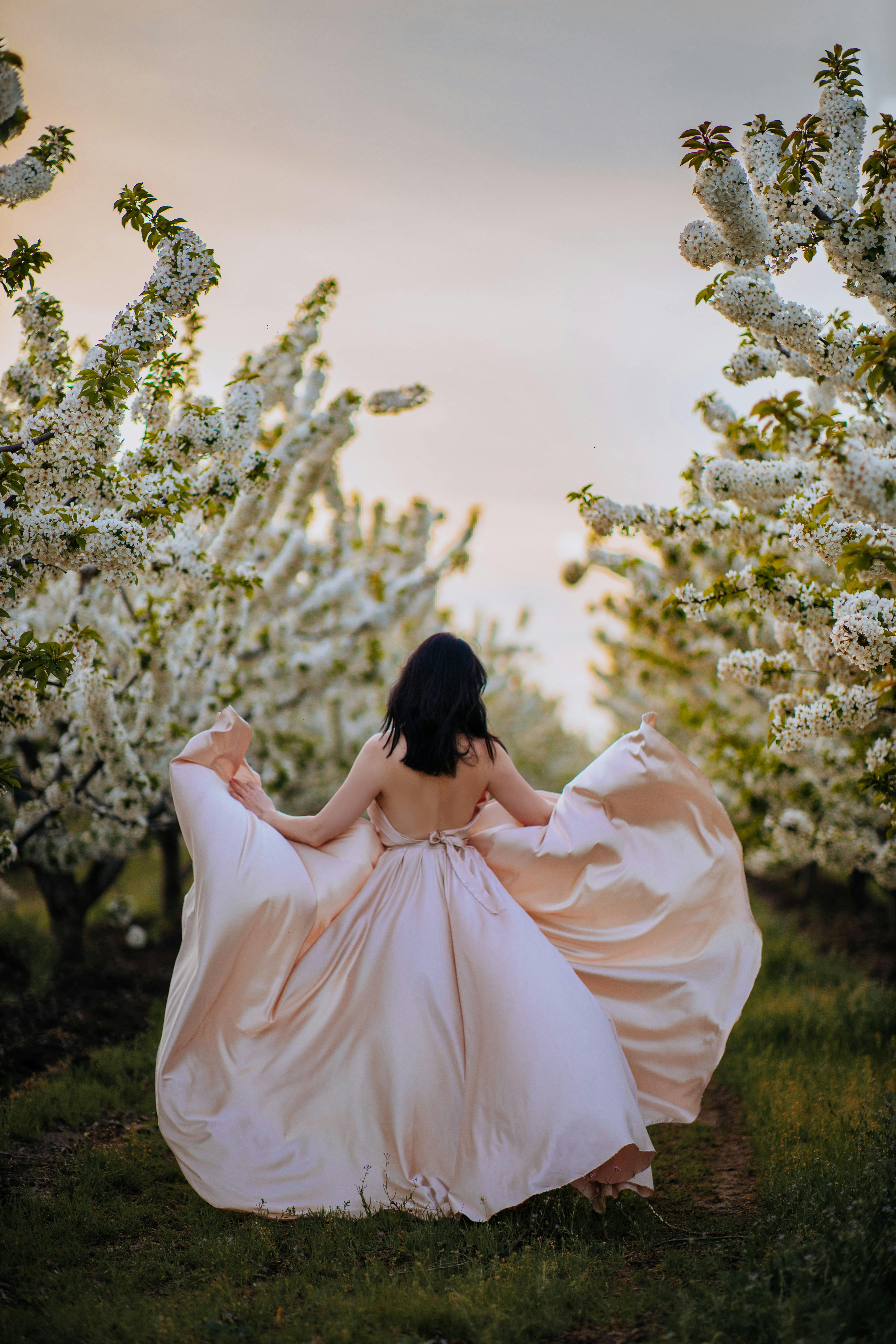 A woman gracefully walks through a blossoming orchard in a flowing peach dress, capturing the essence of spring.