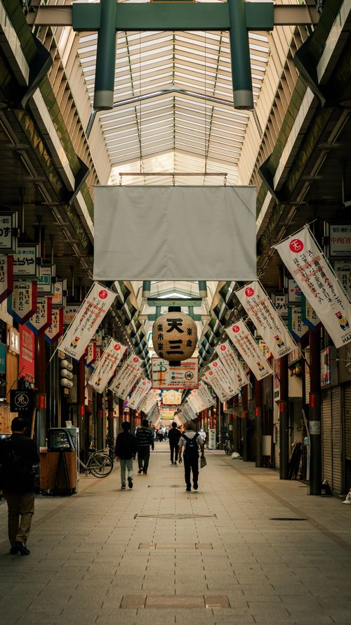 Free Traditional covered shopping arcade in Kyoto with hanging lanterns and pedestrian traffic. Stock Photo